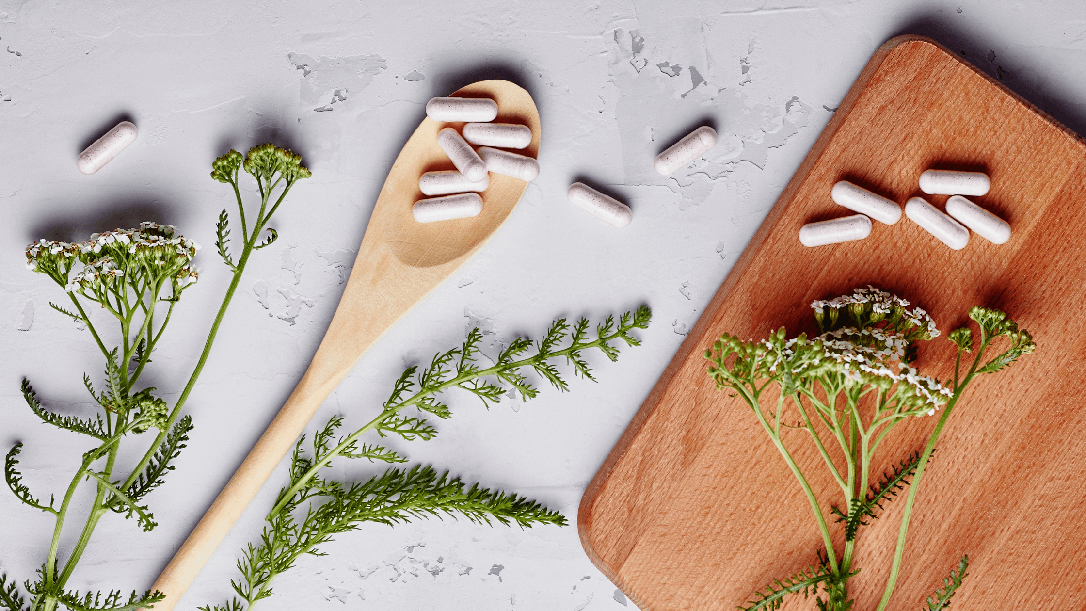 A composition of an array of items related to Naturopathy, artfully arranged, including, sprigs of yarrow, a wooden spoon and cutting board and white pill form supplements to illustrate "PCOS and Pregnancy: Supporting Your Fertility Journey"